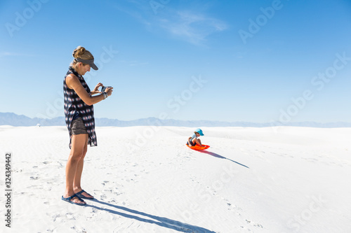 mother taking picture of son sledding on sand dunes,White Sands National Monument photo