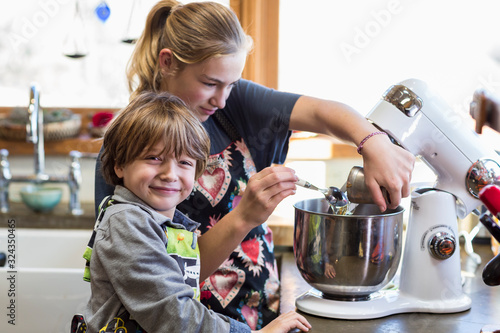 Thirteen year old teenage girl and her 6 year od brother in the kitchen,using a mixing bowl