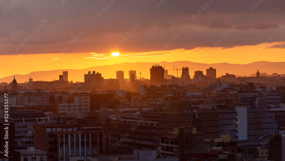 Sunset over the skyline of Barcelona. Silhouettes of buildings in the orange rays of the sun.