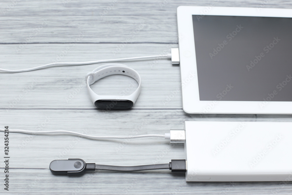 The tablet and tracker are charged from a power bank on a background of wooden boards The tablet and tracker are charged from a power bank on a background of wooden boards