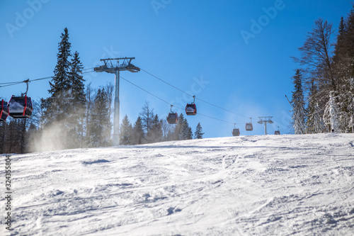 Sunny morning on the mountain, there are not many skiers on the ski slope. The cable car is just above the ski slope and the pine forest is all around.