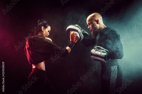 Fototapeta Woman exercising with trainer at boxing and self defense lesson, studio, smoke on background.
