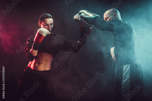 Woman exercising with trainer at boxing and self defense lesson, studio, smoke on background.