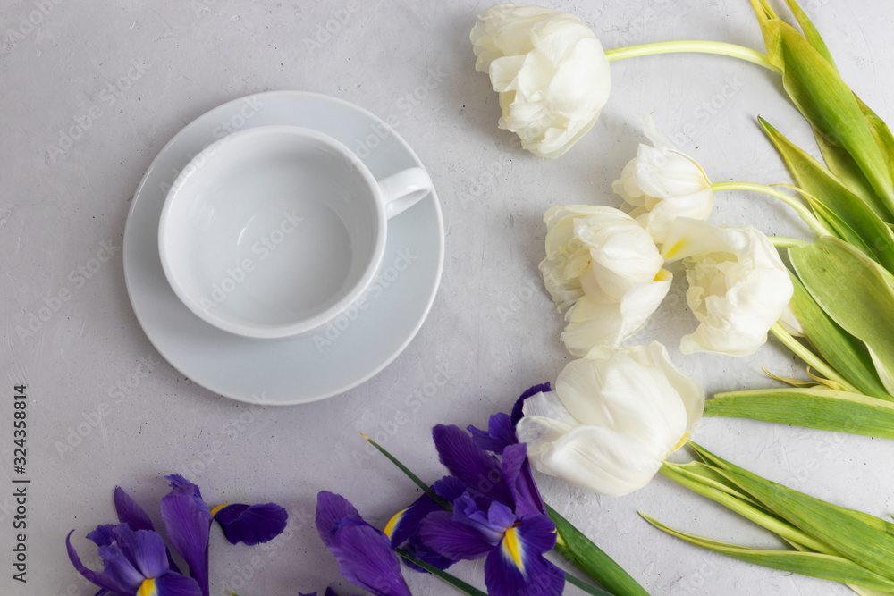 Floral background of live tulips and irises with an empty white cup Floral background of live tulips and irises with an empty white cup