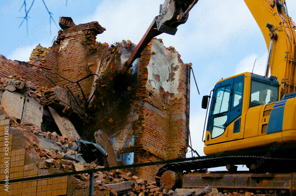 Fototapeta premium A bulldozer destroys an old building. The concept of the demolition of a building under construction of a new house. Dismantling an old house