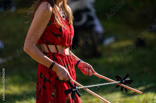 A closeup mid section shallow focus view of a slim caucasian woman entertaining people with devil sticks and flower pendulum at multicultural festival