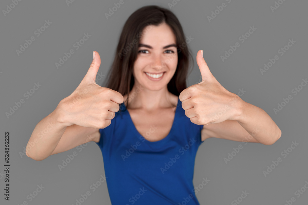 Young girl studio standing isolated on grey thumbs up close-up cheerful blurred backgroud Young girl studio standing isolated on grey thumbs up close-up cheerful blurred backgroud