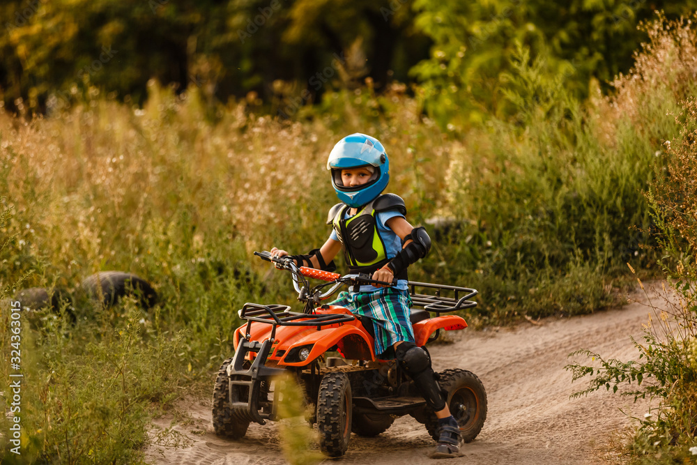 A little boy wearing a helmet riding a quad bike on the shore of a mountain river. A little boy wearing a helmet riding a quad bike on the shore of a mountain river.