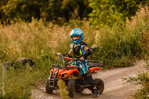 A little boy wearing a helmet riding a quad bike on the shore of a mountain river.