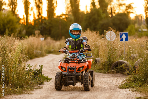 A little boy wearing a helmet riding a quad bike on the shore of a mountain river.