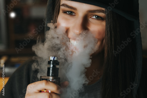 Young pretty woman in cap smoke an electronic cigarette at the vape shop. Hip-hop style. Closeup. photo