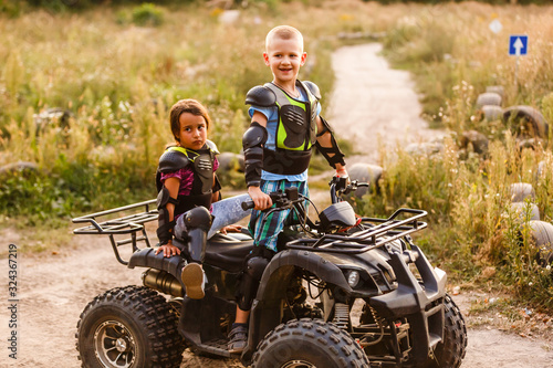 Happy little children playing on road at the day time. They driving on quad bike in the park. Kids having fun on the nature. Concept of happiness. © Angelov