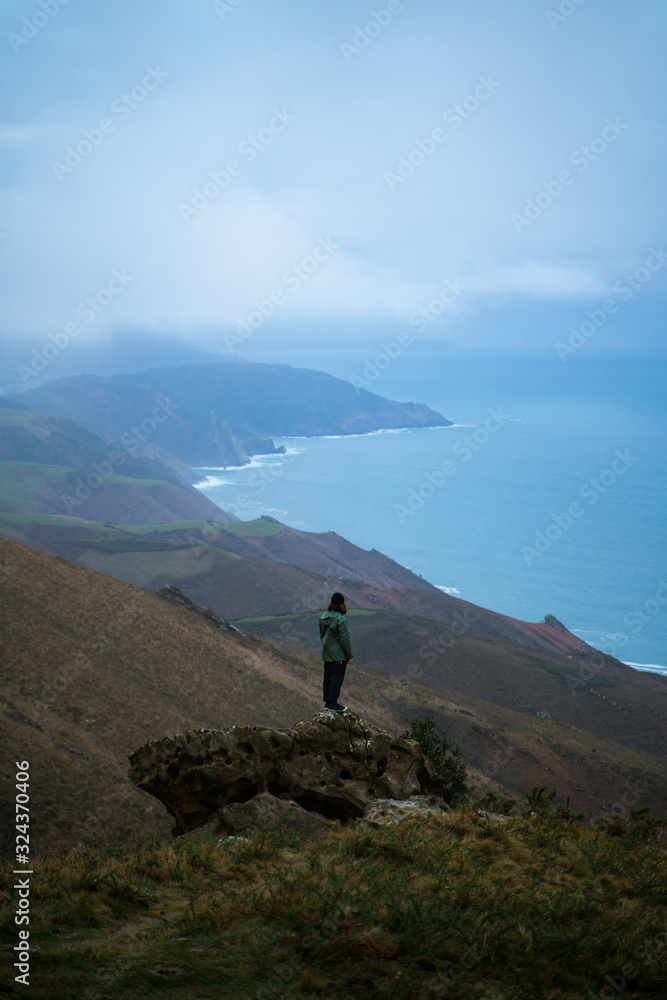 Plakat Man standing on top of a big rock contemplating the views from the top of Basque Country coast