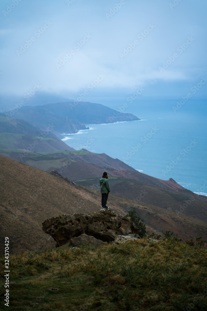 Man standing on top of a big rock contemplating the views from the top of Basque Country coast