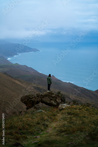 Man standing on top of a big rock contemplating the views from the top of Basque Country coast