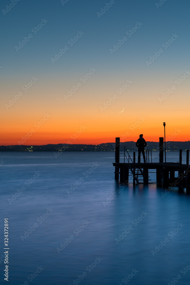 A man silhouette standing on wooden pier lonely at the sea with beautifulsunset. lsunset seascape at a wooden jetty