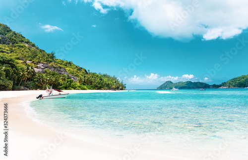 Amazing tropical beach with white untouched sand, turquoise ocean with sailing and motor yachts and beautiful exotic island at background. Summer vacation background