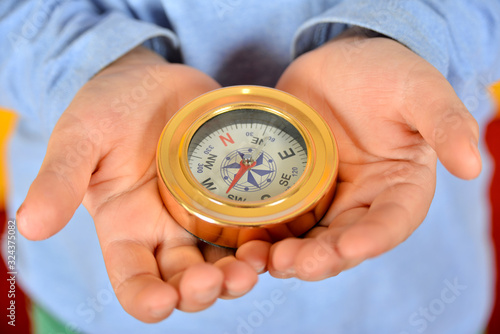 The child holds a compass in his hands and looks at the direction of the arrow.