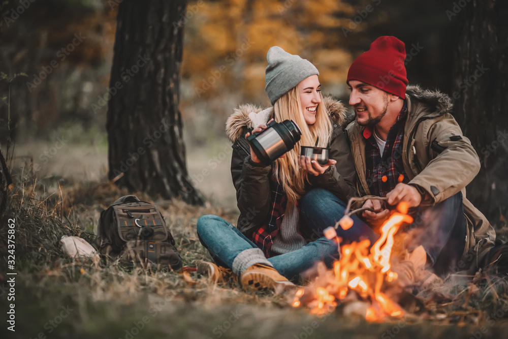 Traveler couple camping and roasting marshmallows over the fire in the forest after a hard day. Concept of trekking, adventure and seasonal vacation. Traveler couple camping and roasting marshmallows over the fire in the forest after a hard day. Concept of trekking, adventure and seasonal vacation.