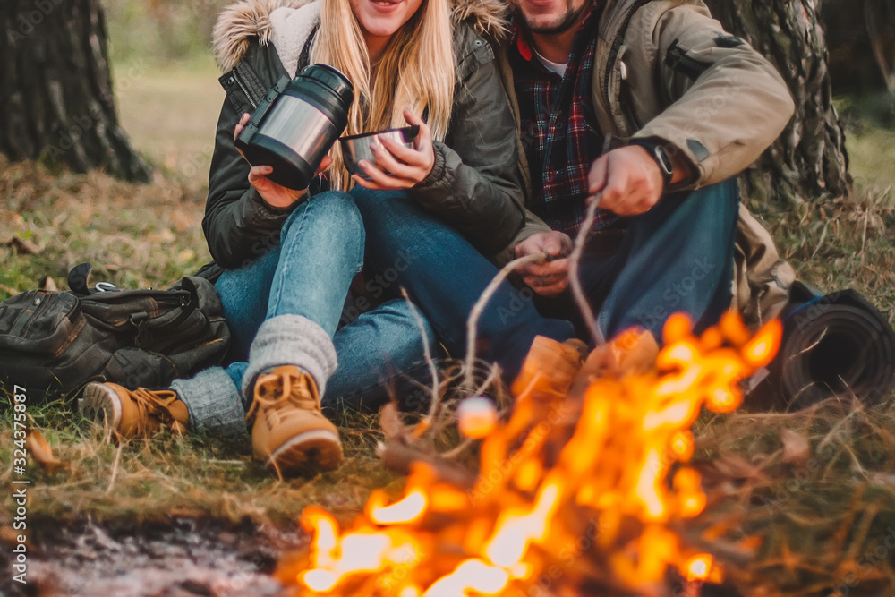 Traveler couple camping and roasting marshmallows over the fire in the forest after a hard day. Concept of trekking, adventure and seasonal vacation. Traveler couple camping and roasting marshmallows over the fire in the forest after a hard day. Concept of trekking, adventure and seasonal vacation.