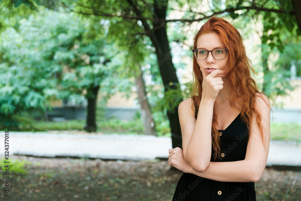 Pensive girl student in glasses walks in park. Ginger girl outdoor, copyspace. Pensive girl student in glasses walks in park. Ginger girl outdoor, copyspace.