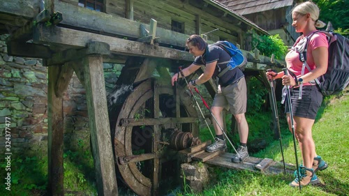 A couple of hikers stop to admire an old water mill at Prevalje, Slovenia photo