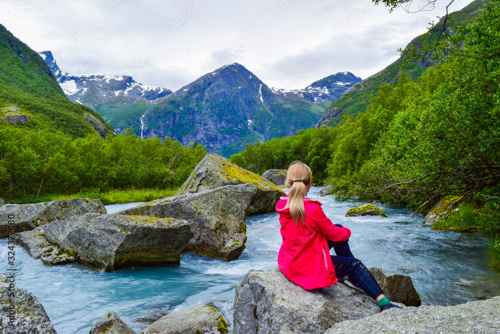 The young woman near river which is located near path to the Briksdalsbreen (Briksdal) glacier. The melting of this glacier forms waterfall and river with clear water. Jostedalsbreen National Park. No The young woman near river which is located near path to the Briksdalsbreen (Briksdal) glacier. The melting of this glacier forms waterfall and river with clear water. Jostedalsbreen National Park. No