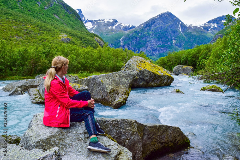 The young woman near river which is located near path to the Briksdalsbreen (Briksdal) glacier. The melting of this glacier forms waterfall and river with clear water. Jostedalsbreen National Park. No The young woman near river which is located near path to the Briksdalsbreen (Briksdal) glacier. The melting of this glacier forms waterfall and river with clear water. Jostedalsbreen National Park. No