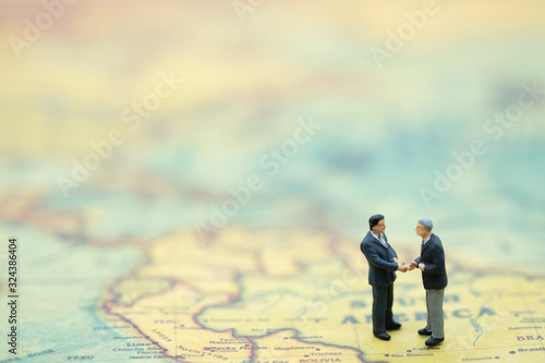Two businessman miniature people figures meeting and hand shake on world map background with copy space. Using as business, financial, money and cooperation concept.