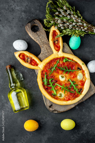 Festive Easter pizza in the form of a rabbit with eggs, multi-colored  Easter eggs on a stone background. Easter celebration concept.