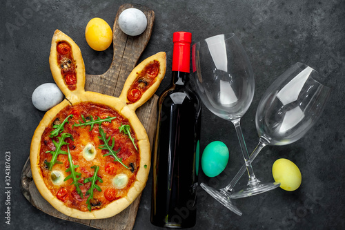 Concept  celebrations  Easter. Festive Easter rabbit pizza with eggs on a cutting board with a bottle of wine and glasses on a stone background