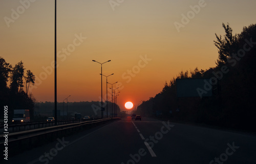 Beautiful view of sunrise over the asphalted road with cars stretching off past trees in the early morning.