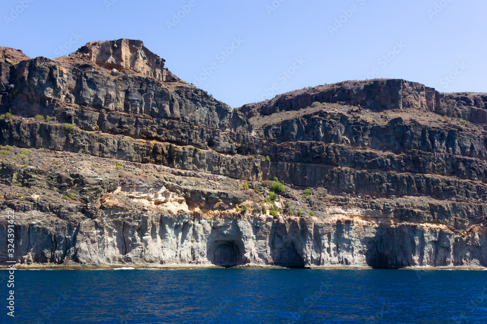 Gran Canaria arid rocky mountains view with caves by the sea. Desert landscape by ocean in Canary Islands, Spain. Boat trip, summer vacation concepts