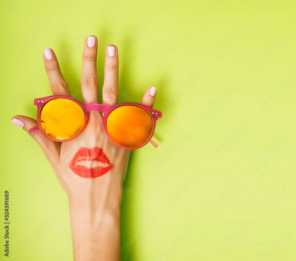 Fototapeta woman hand holding sunglasses on bright green background, cosmetic or vacation concept