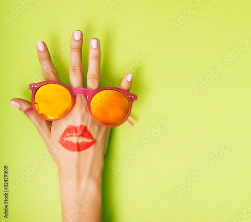 Fototapeta woman hand holding sunglasses on bright green background, cosmetic or vacation concept