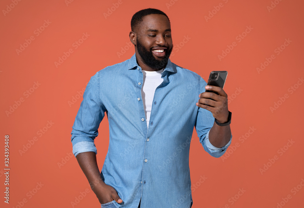 Handsome man using smartphone, checks for new message. Photo of african man in casual outfit on coral background.
