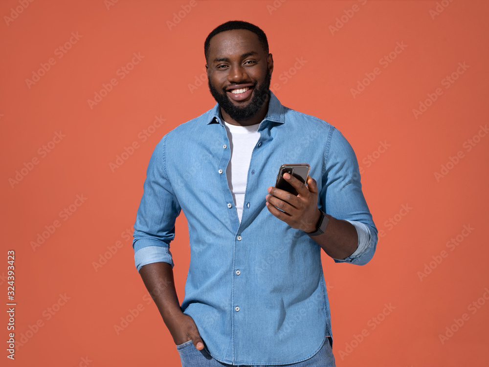 Handsome man using smartphone. Photo of african man in casual outfit on coral background. Handsome man using smartphone. Photo of african man in casual outfit on coral background.