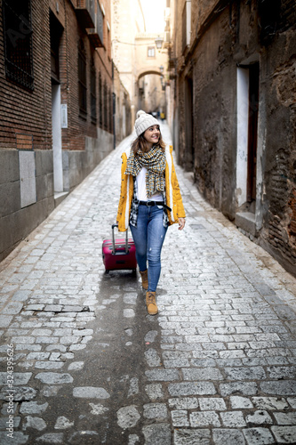 young girl sightseeing through the streets of a city with yellow coat, wool cap and suitcase