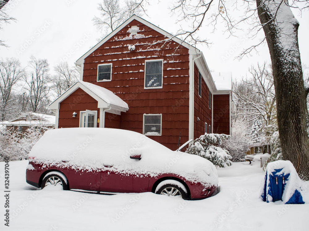 red car in front of red suburban house during the snow storm red car in front of red suburban house during the snow storm