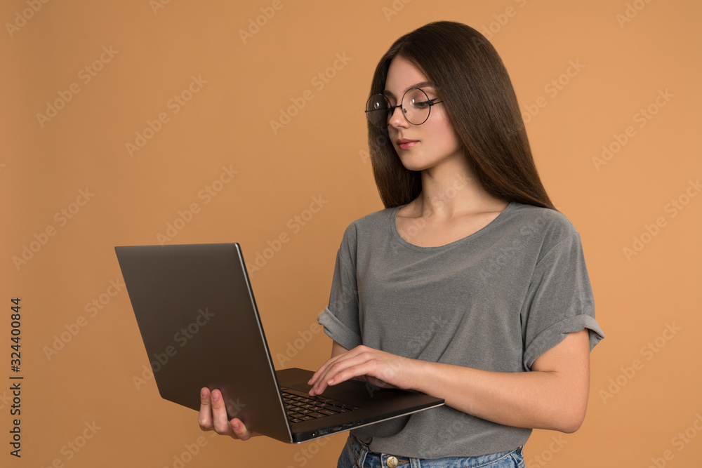 Naklejka premium Confident brunette business lady with laptop in her hands, female in glasses holds her hand on the keyboard and looking at the display
