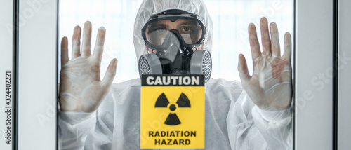 scientist with coverall protection clothing and full face protection mask in control room with radiation hazard sign photo