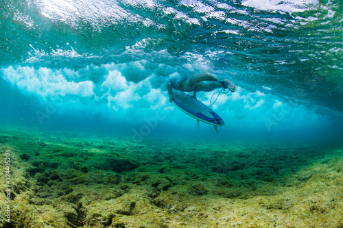Surfer duckdiving a wave over a shallow coral reef