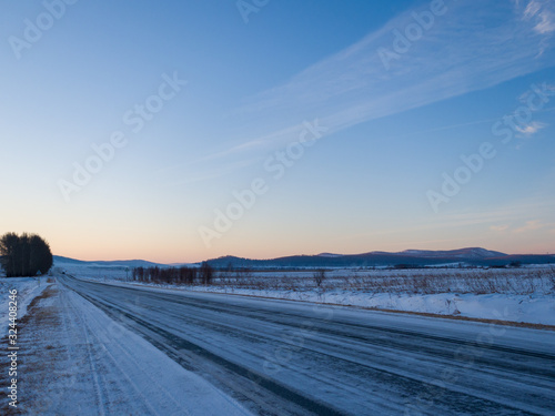 Panorama of the highway in winter Siberia. Sunrise over a snowy plain. Beautiful sky