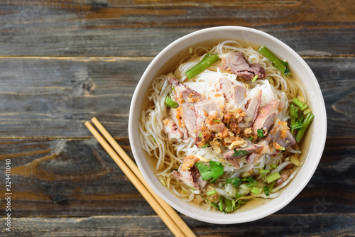 Rice noodles soup with beef in a bowl and chopsticks on wooden background, Asian food, Top view photo