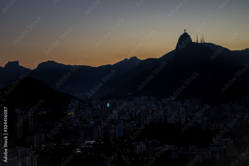 View of Christ the redeemer (Cristo Redentor) as silhouette on top of Mount Corcovado just after sunset at nightfall with city lights in Rio de Janeiro, South America
