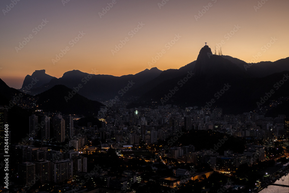 View of Christ the redeemer (Cristo Redentor) as silhouette on top of Mount Corcovado just after sunset at nightfall with city lights in Rio de Janeiro, Brazil, South America