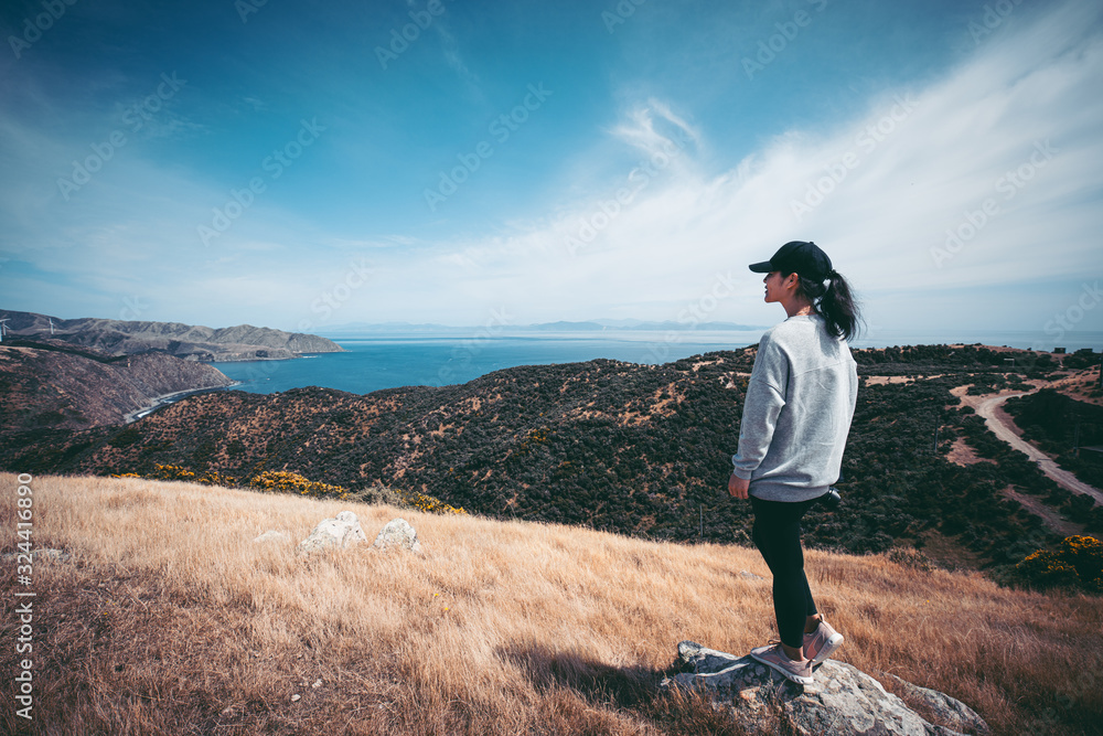 Naklejka premium Woman photographer hiking on Makara beach, Wellington, NZ