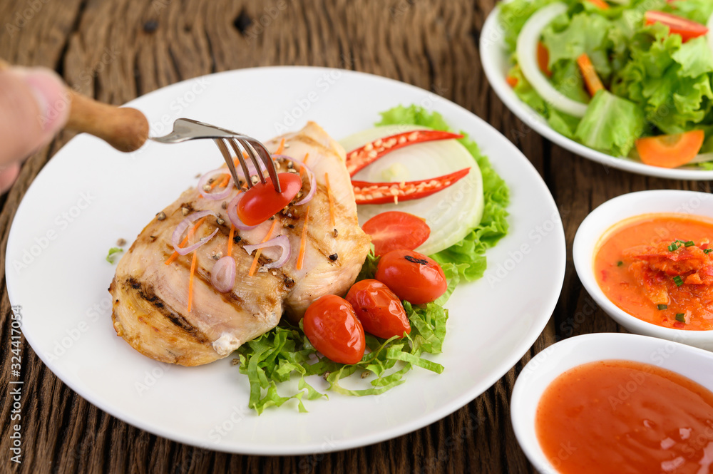 Grilled chicken on a white plate with tomatoes, salad, onion, chili and sauce.