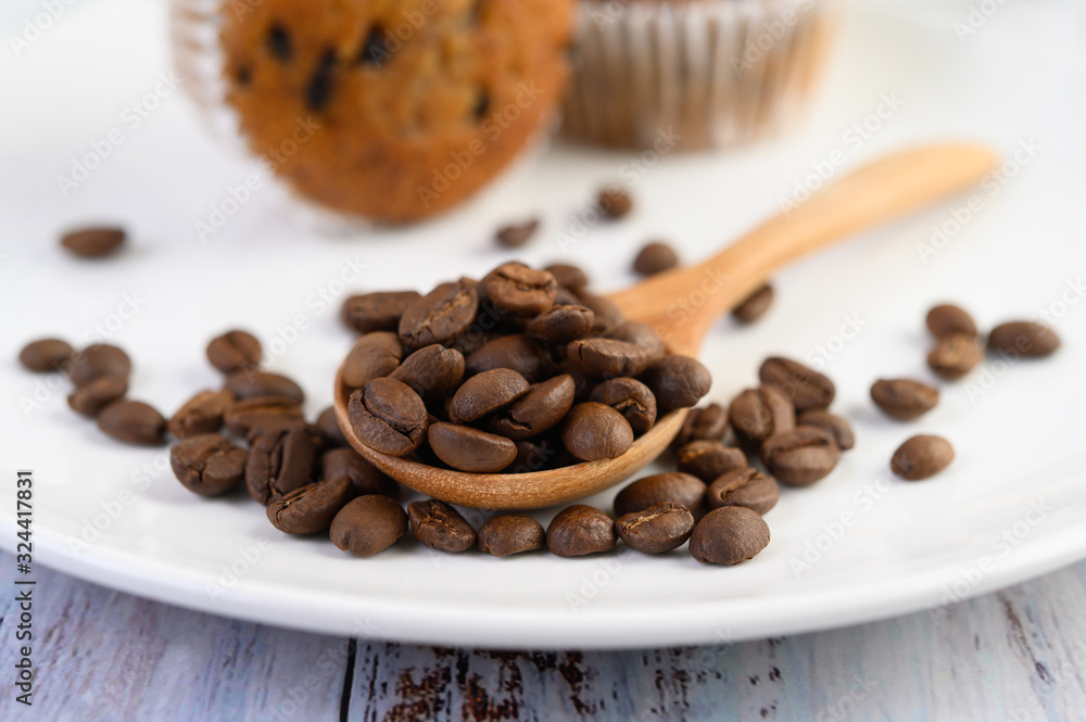 Fototapeta premium Coffee beans on wooden spoon and Banana Cupcakes on a white wood table.