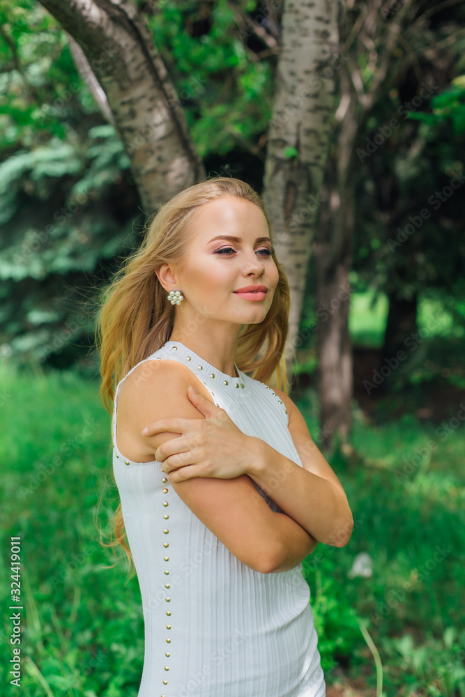 Portrait of a charming blond woman wearing beautiful white dress standing next to rowan tree. Portrait of a charming blond woman wearing beautiful white dress standing next to rowan tree.